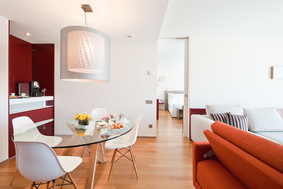 Un espacio habitable moderno con una mesa de comedor de vidrio, sillas blancas, un sofá rojo y una lámpara colgante grande.