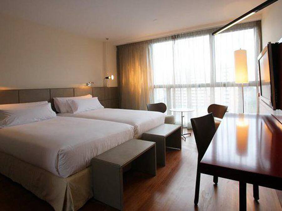 Habitación de hotel con dos camas, un escritorio, una silla y un televisor.