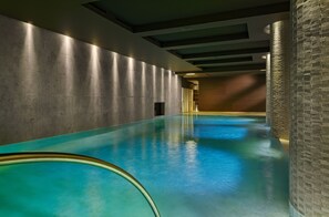 Uma piscina interior comprida e estreita com fundo de vidro, rodeada por paredes com acabamento texturizado.