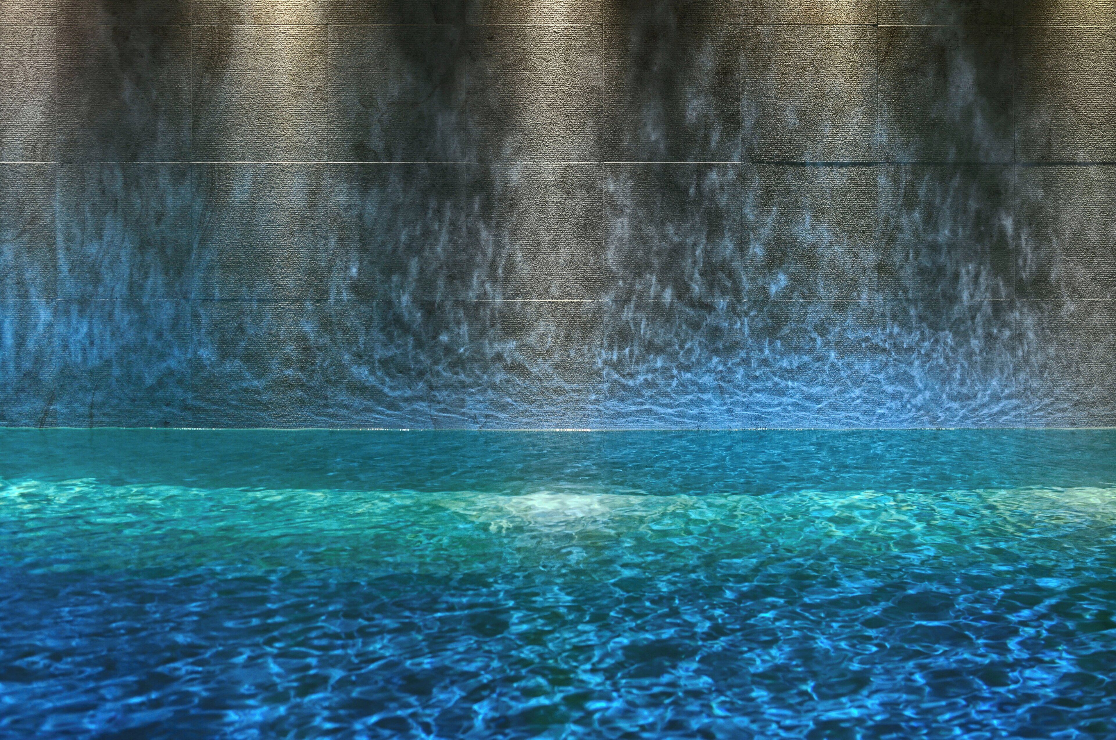 A pool with clear water and a textured wall in the background.