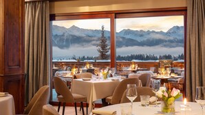Ein Restaurant mit gedeckten Tischen, großen Fenstern mit Bergblick und einer gemütlichen Einrichtung.