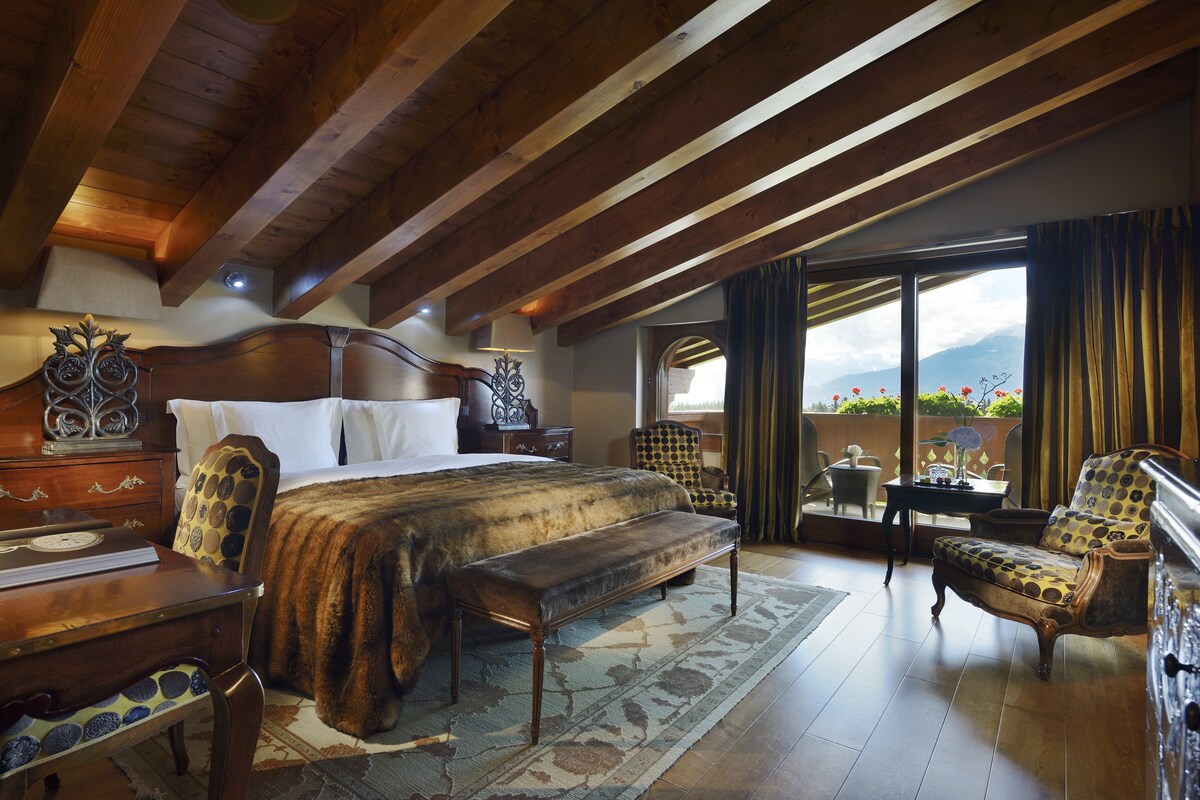 A bedroom with a large bed, a bench, a wooden dresser, a chair, and a view of the outdoors.