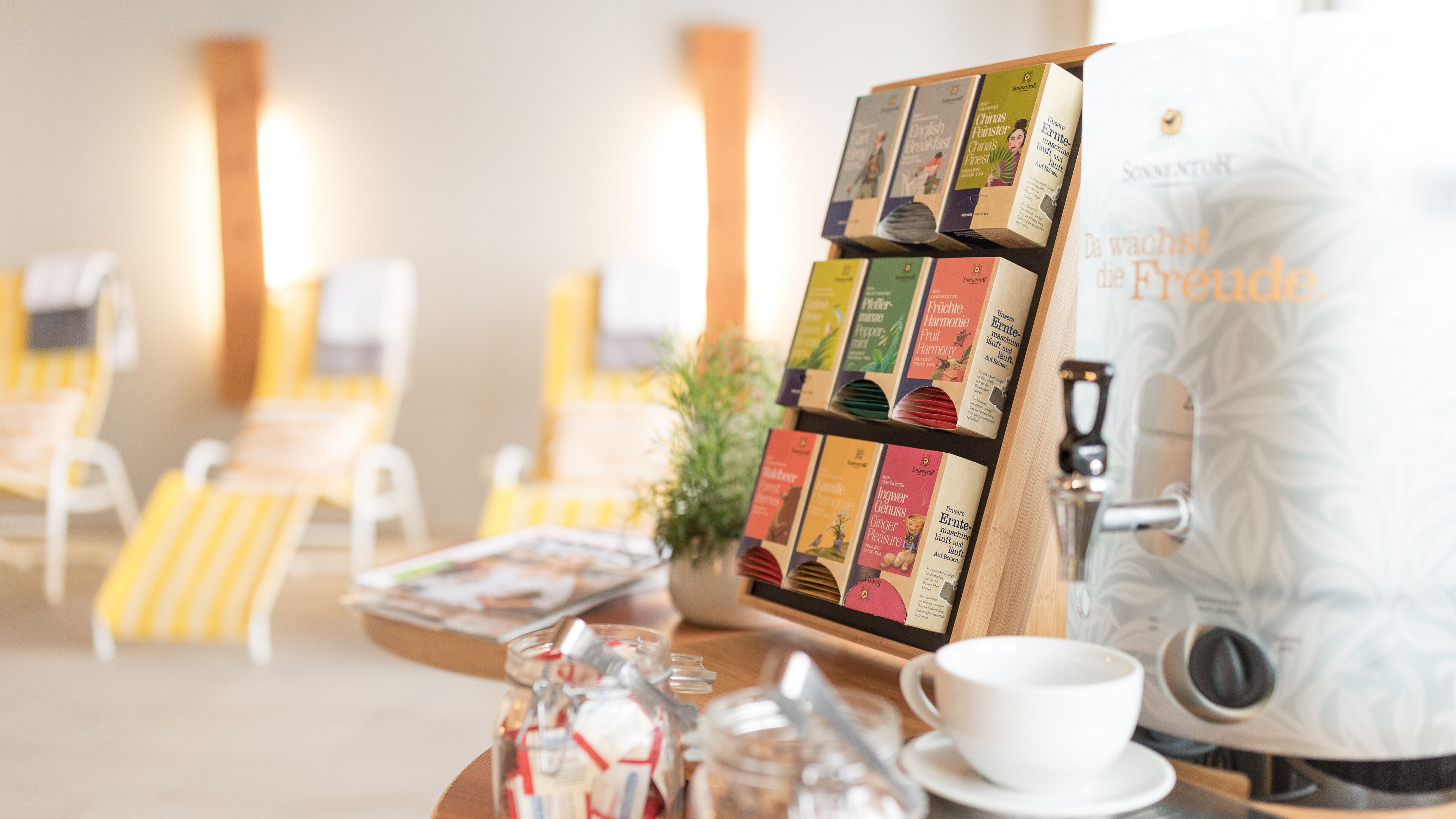 Una cafetera con variedad de cápsulas de té y café, una taza y una bandeja con utensilios.