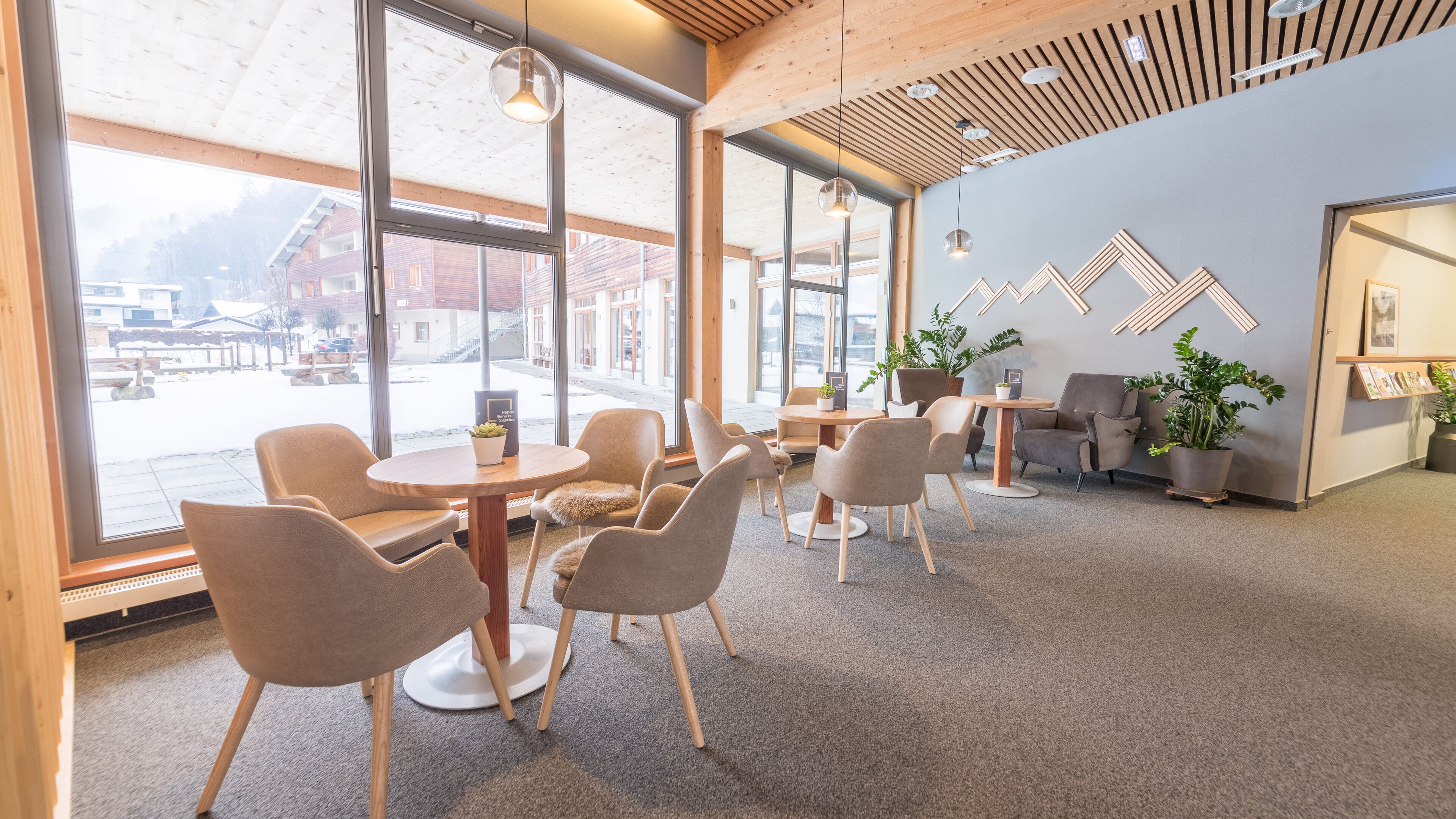 A modern interior with large windows, wooden ceiling, and a seating area with round tables and chairs.