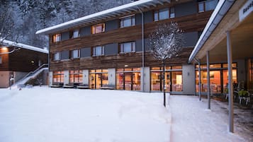 Ein modernes Gebäude mit Holzfassade, großen Fenstern und einer überdachten Außenbereits mit Sitzgelegenheiten.