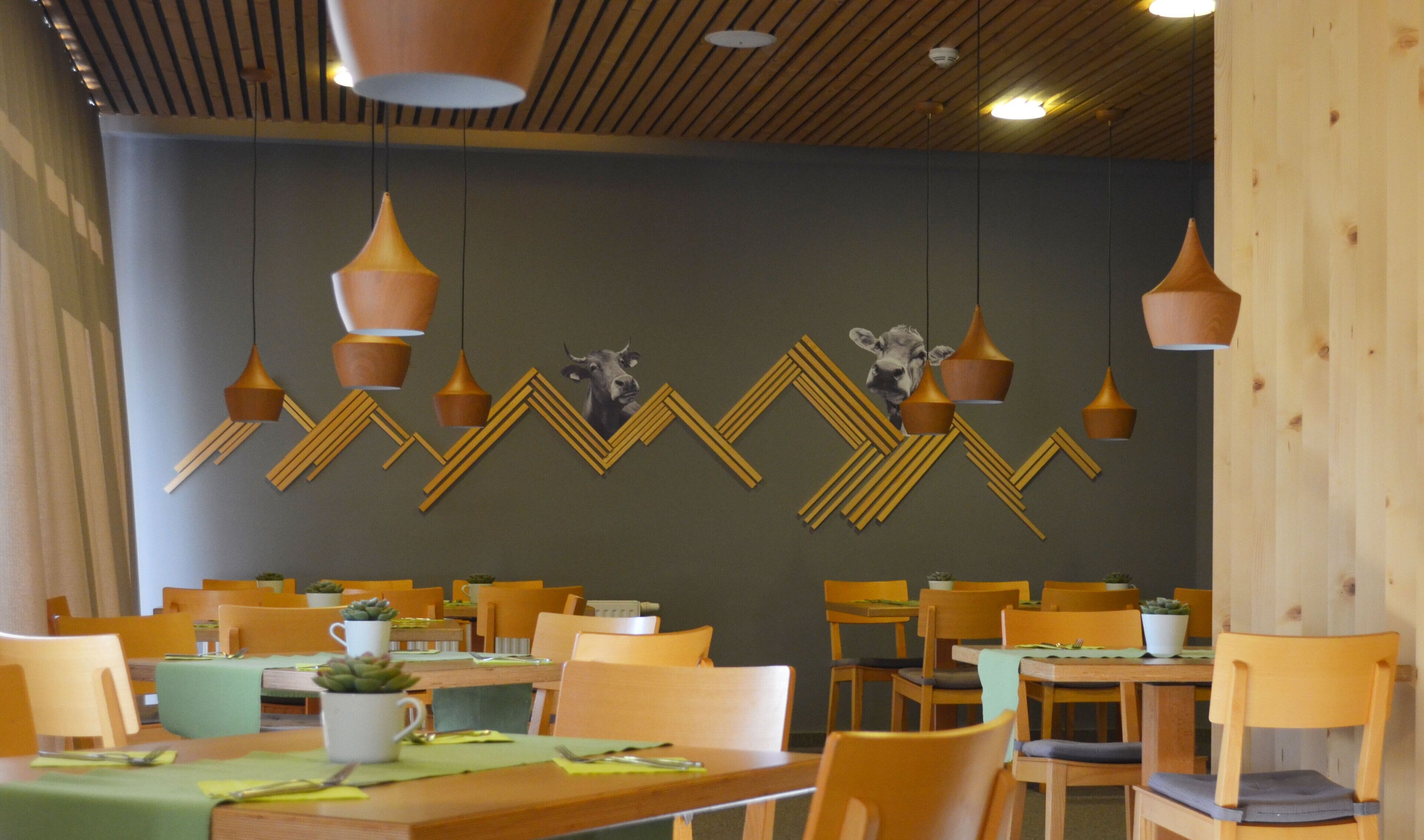 Ein Restaurant mit Holztischen und -stühlen, hängenden Pendelleuchten und einem geometrischen Wanddesign.