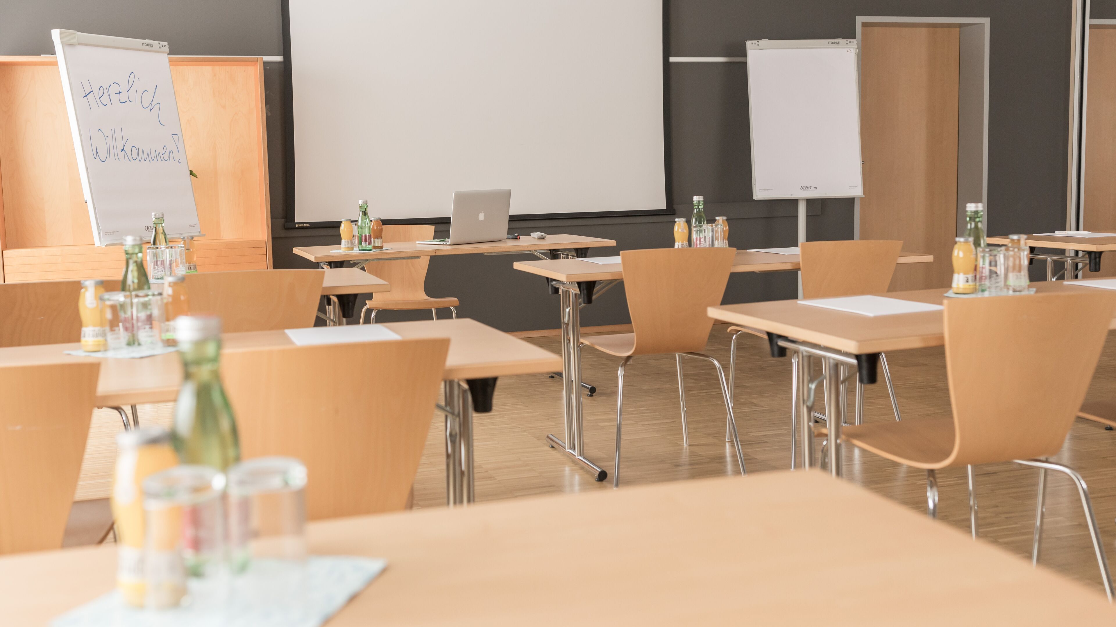 Een klaslokaal met houten tafels, stoelen en een whiteboard.