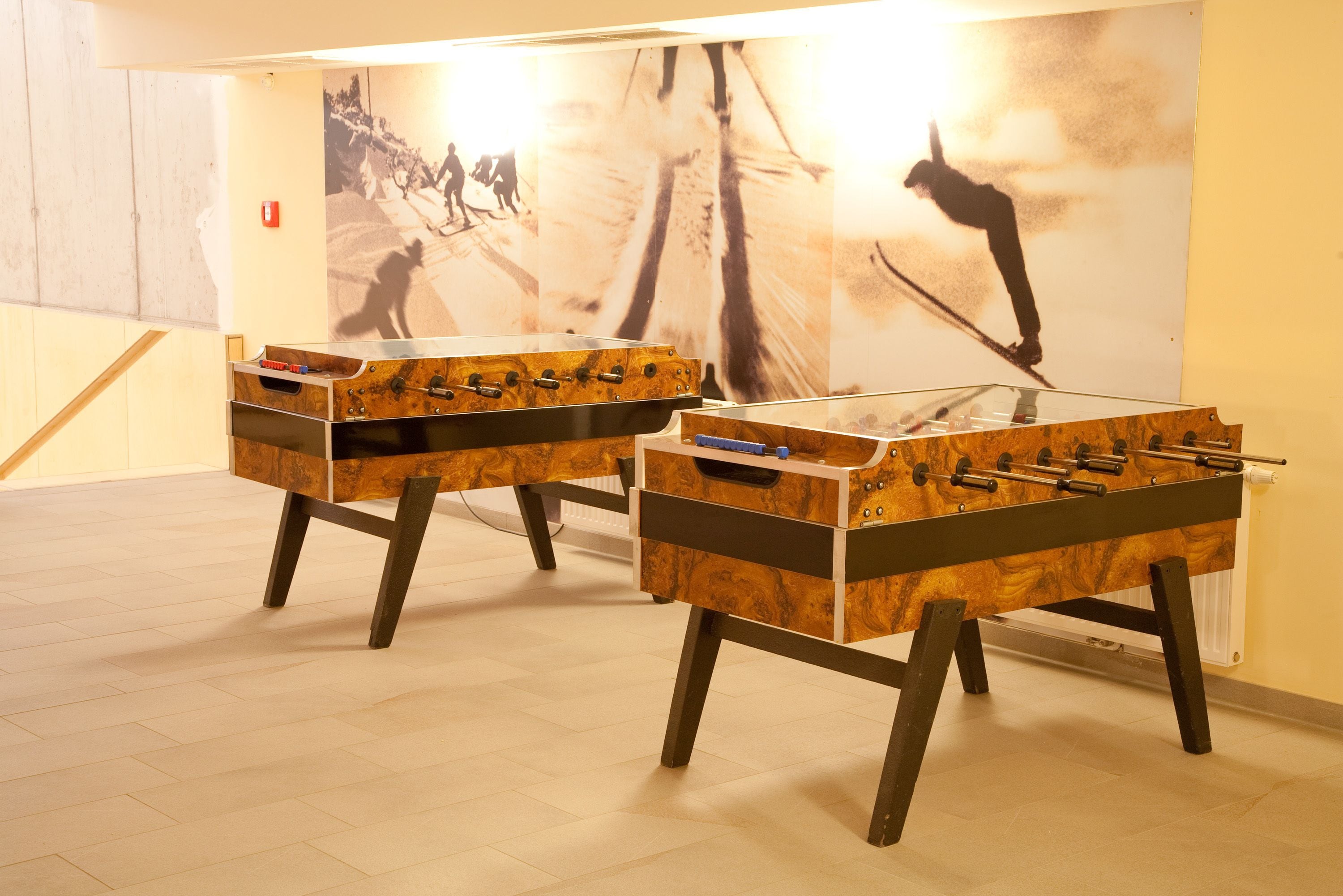 Two foosball tables in a room with a wooden floor and a large wall mural.