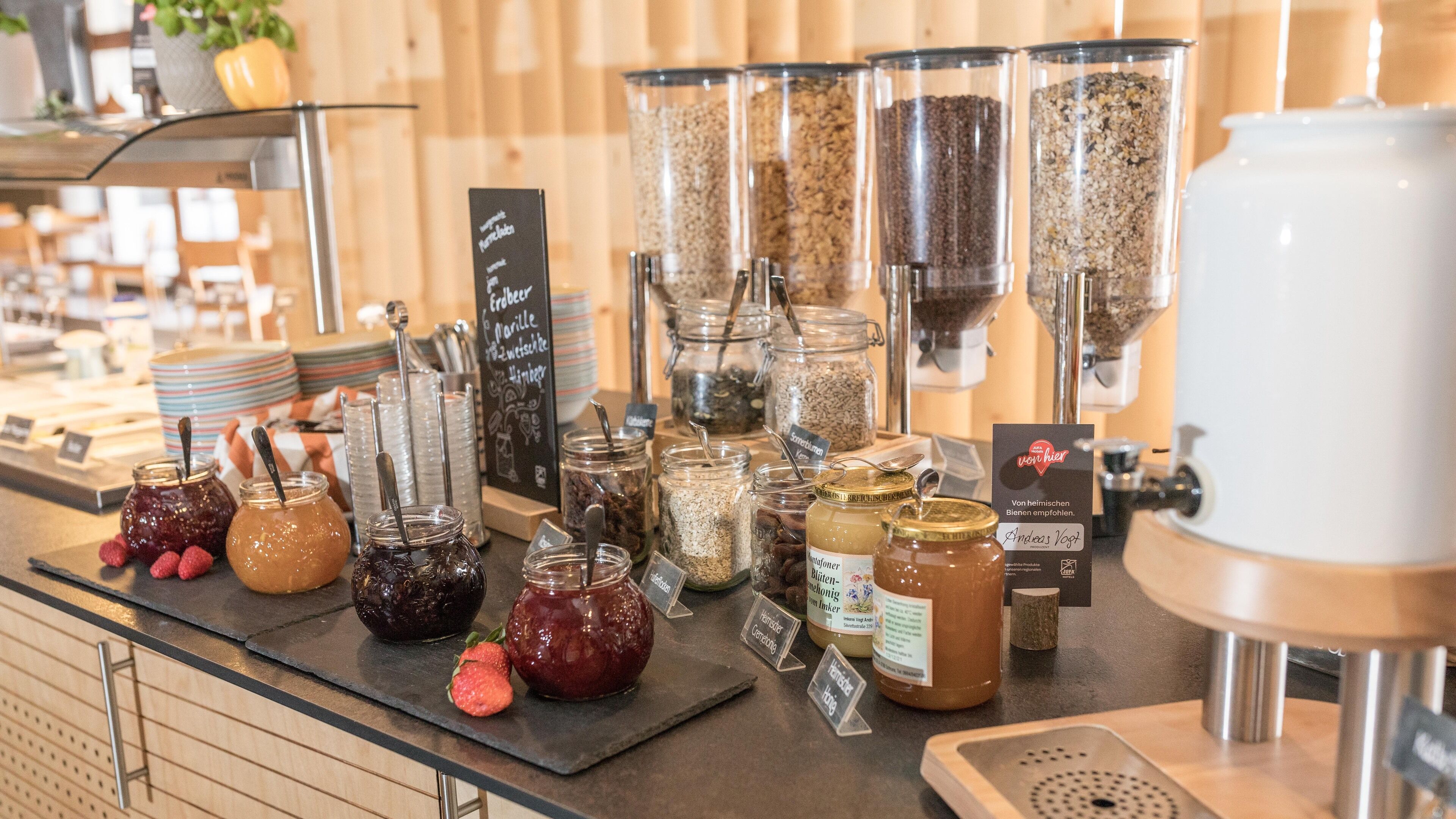 A food display with various jars of preserves and grains, a coffee machine, and a chalkboard menu.