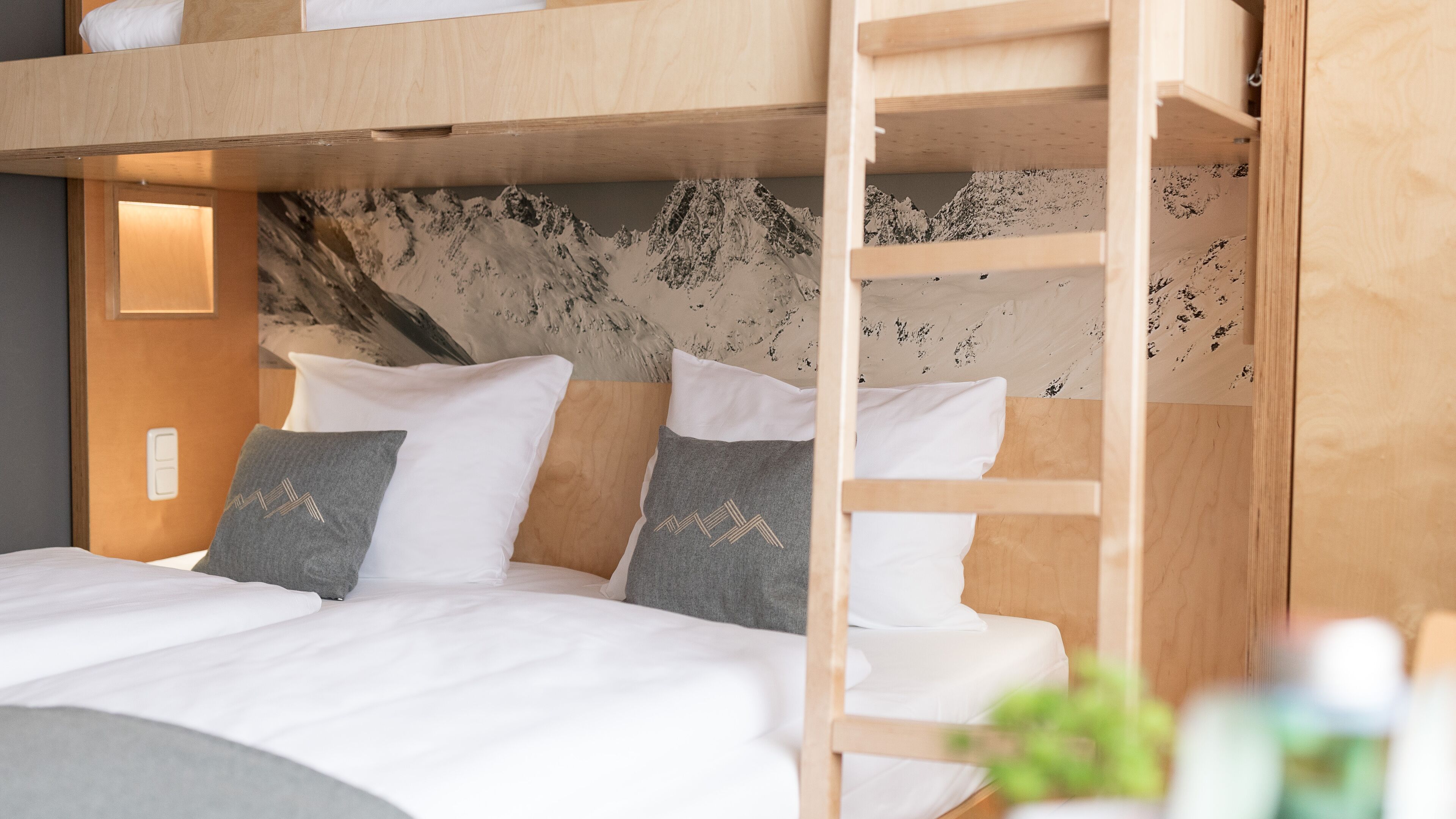 A bunk bed with white bedding and grey pillows, a wooden headboard, and a wall with a textured, abstract design.