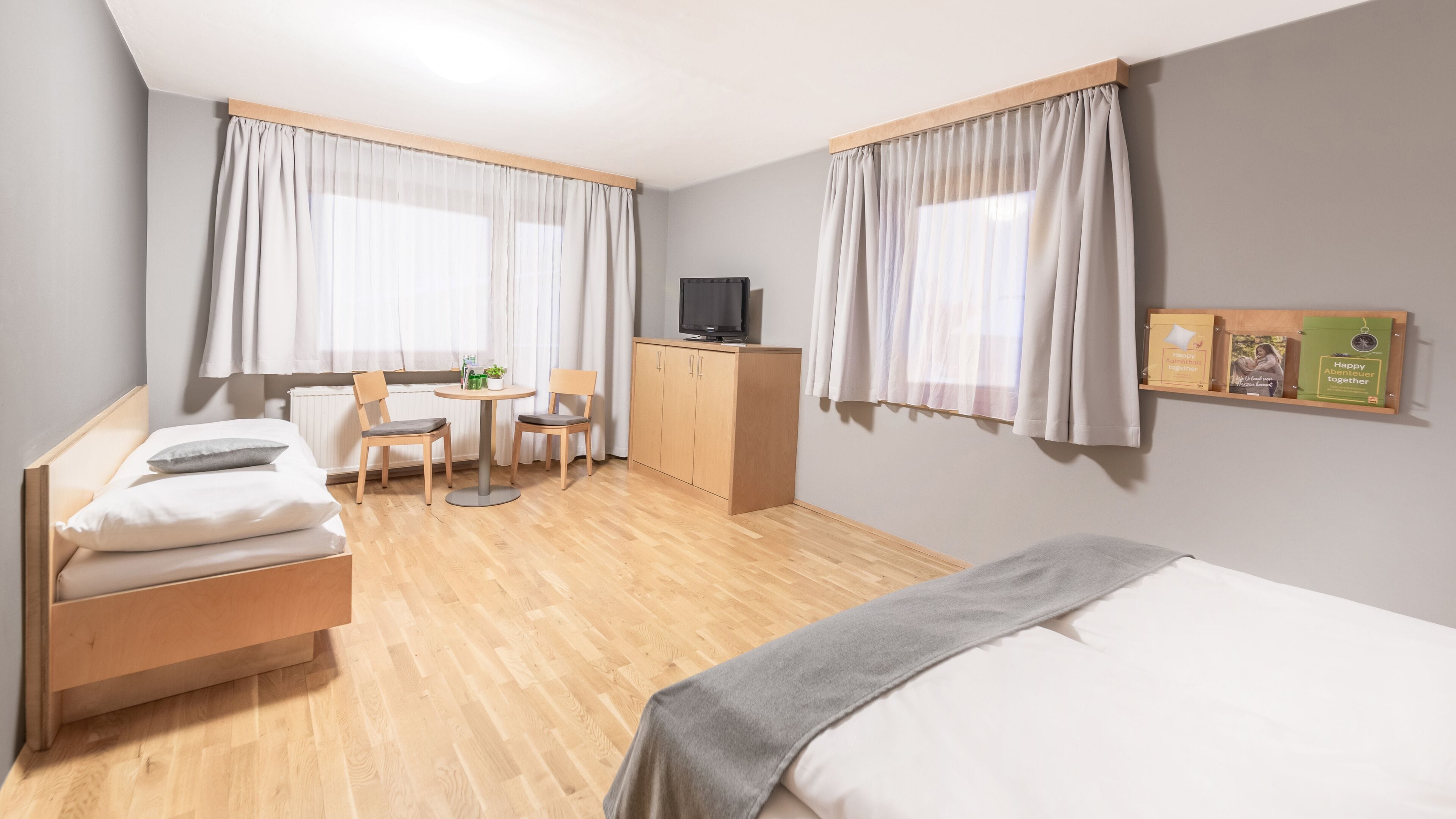 Habitación de hotel con cama, escritorio con televisor, dos sillas, una mesita y un armario.