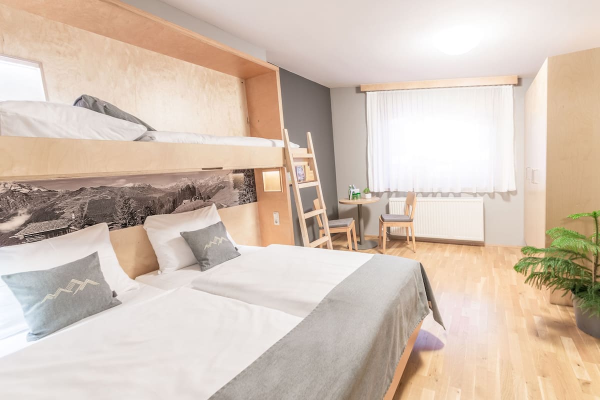 A bedroom with a bunk bed, a desk, a chair, a radiator, and a potted plant.