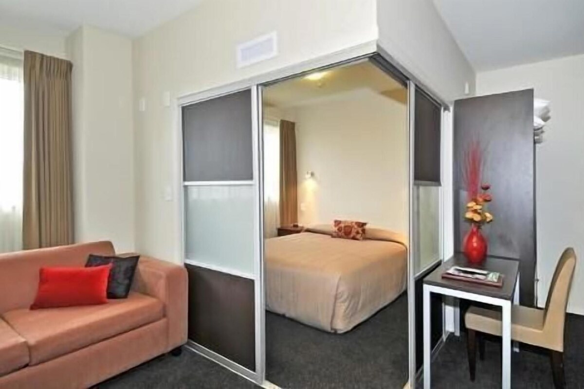 A hotel room with a bed, a sofa, a small table with a vase, and a chair.