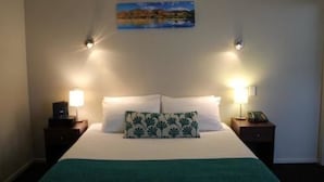 A hotel room with a bed, two bedside lamps, a nightstand with a phone, and a painting on the wall. - 540 on Great South Motel (Auckland)