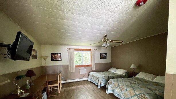 A room with two beds, a desk, a chair, a television, and a ceiling fan. - The Riverside Inn (Stowe)