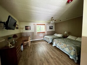 A room with two beds, a desk, a chair, a television, and a ceiling fan. - The Riverside Inn (Stowe)