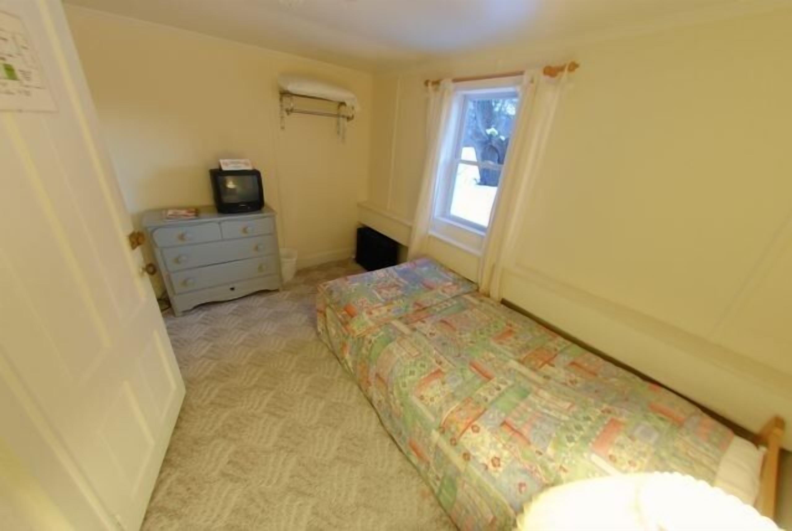 A small bedroom with a single bed, a dresser, a television, and a window.