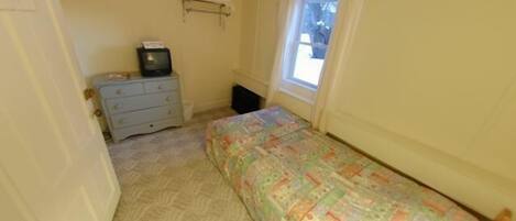 A small bedroom with a single bed, a dresser, a television, and a window.