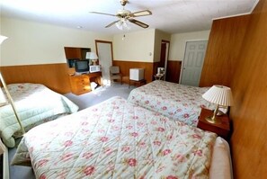 Habitación de hotel con dos camas, un escritorio con computadora, una silla, televisor y ventilador de techo.