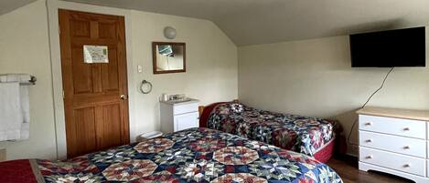 Un dormitorio con una cama grande, un aparador, un televisor montado en la pared y una puerta.