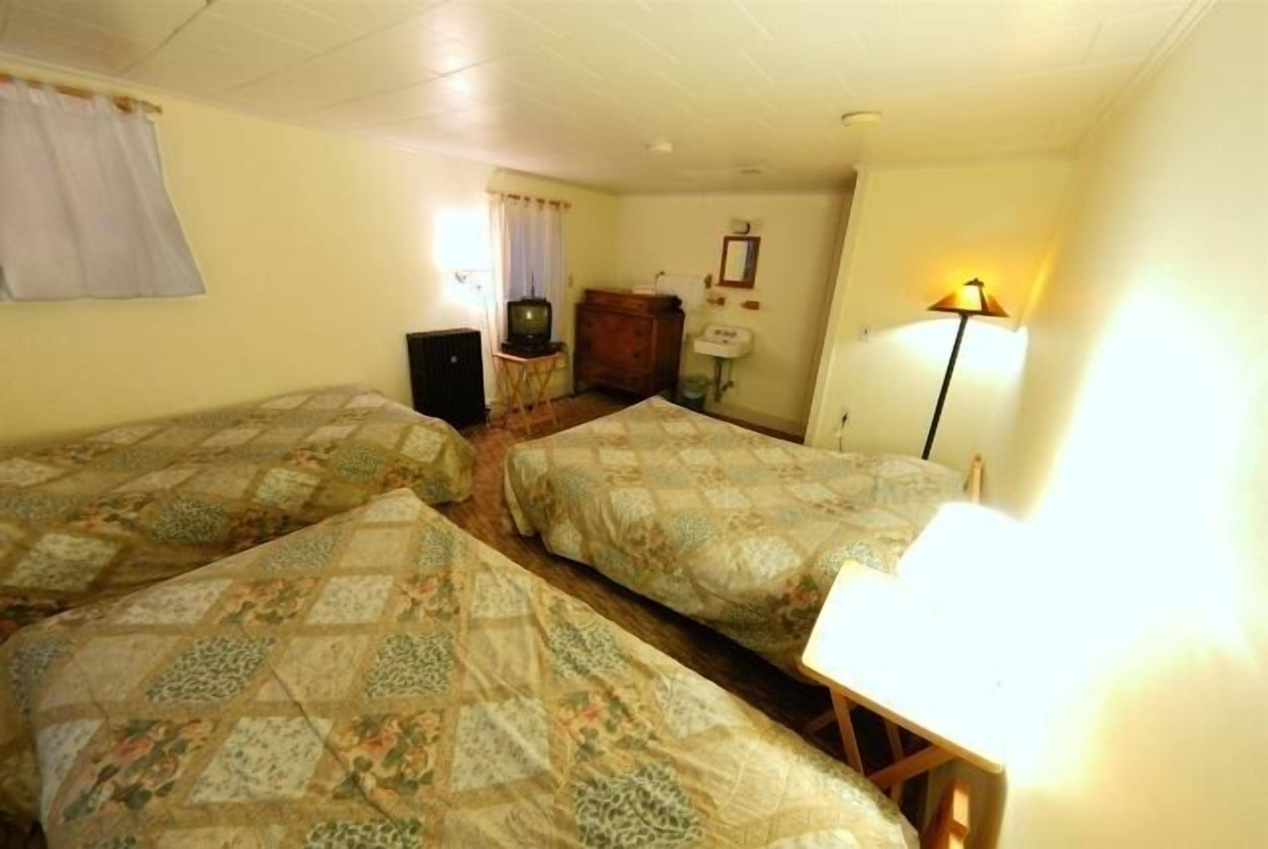 A room with two beds, a small table, a lamp, a television, and a dresser.