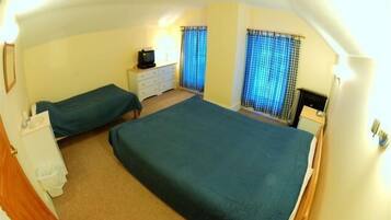 A room with two beds, a small bedside table with a lamp, and a dresser.
