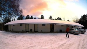 A snow-covered building with a curved roof, a person walking in the snow, and a car parked nearby. - The Riverside Inn (Stowe)
