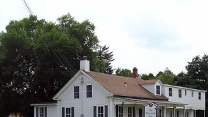 A white two-story building with a porch and a sign that reads "The Riverside Inn." - The Riverside Inn (Stowe)