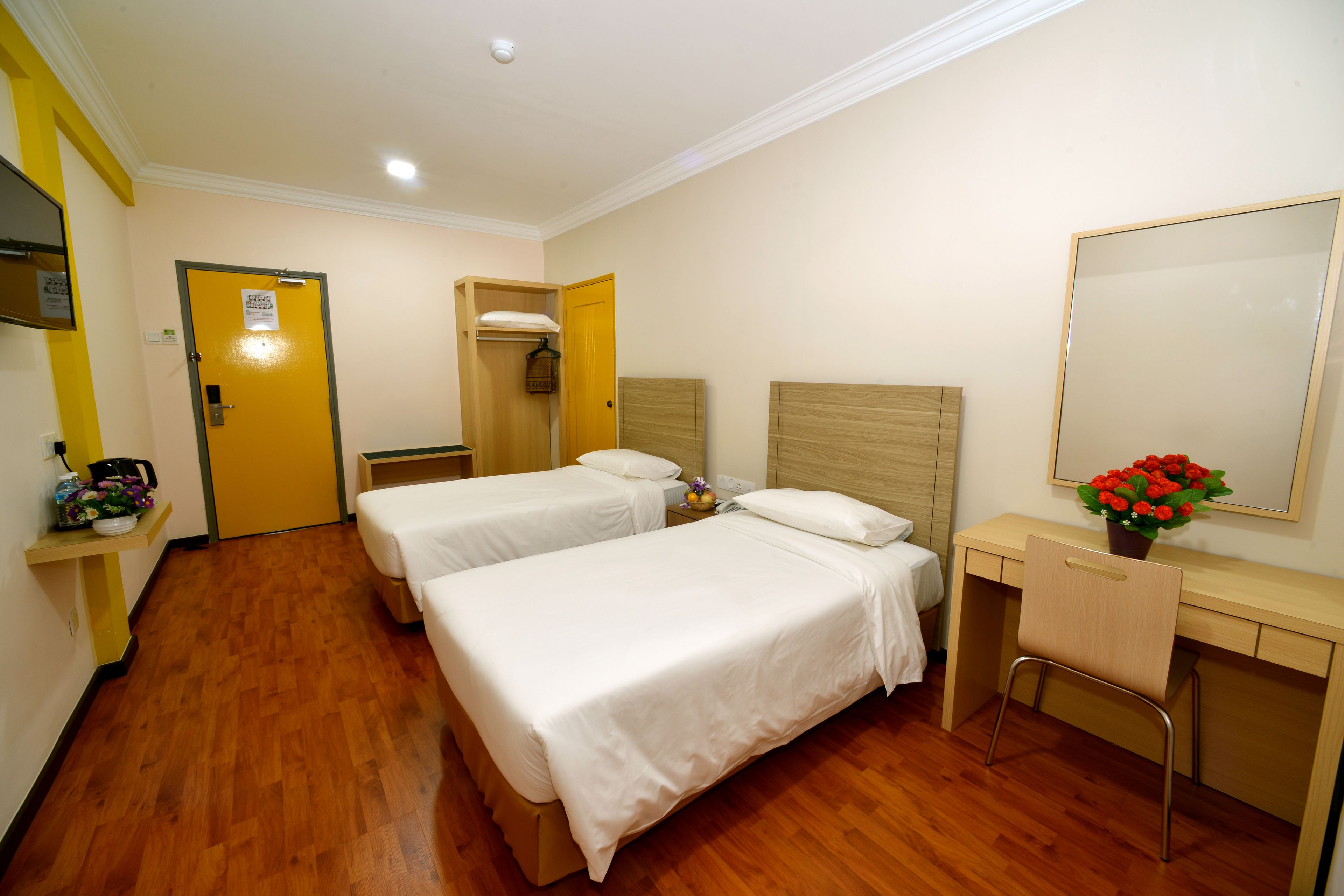 Ein Hotelzimmer mit zwei Betten, einem Schreibtisch, einem Stuhl, einem Spiegel und einer Tür.