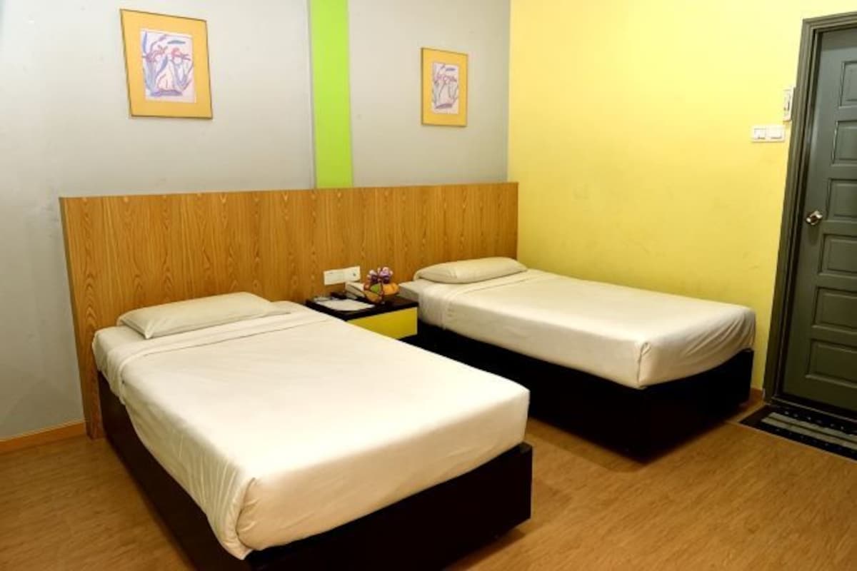 A room with two beds, a wooden headboard, a nightstand with a lamp, and a door.