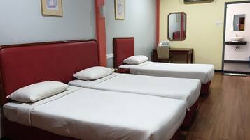 A hotel room with two single beds, a desk with a chair, a small table, a mirror, and a bathroom with a sink and mirror.