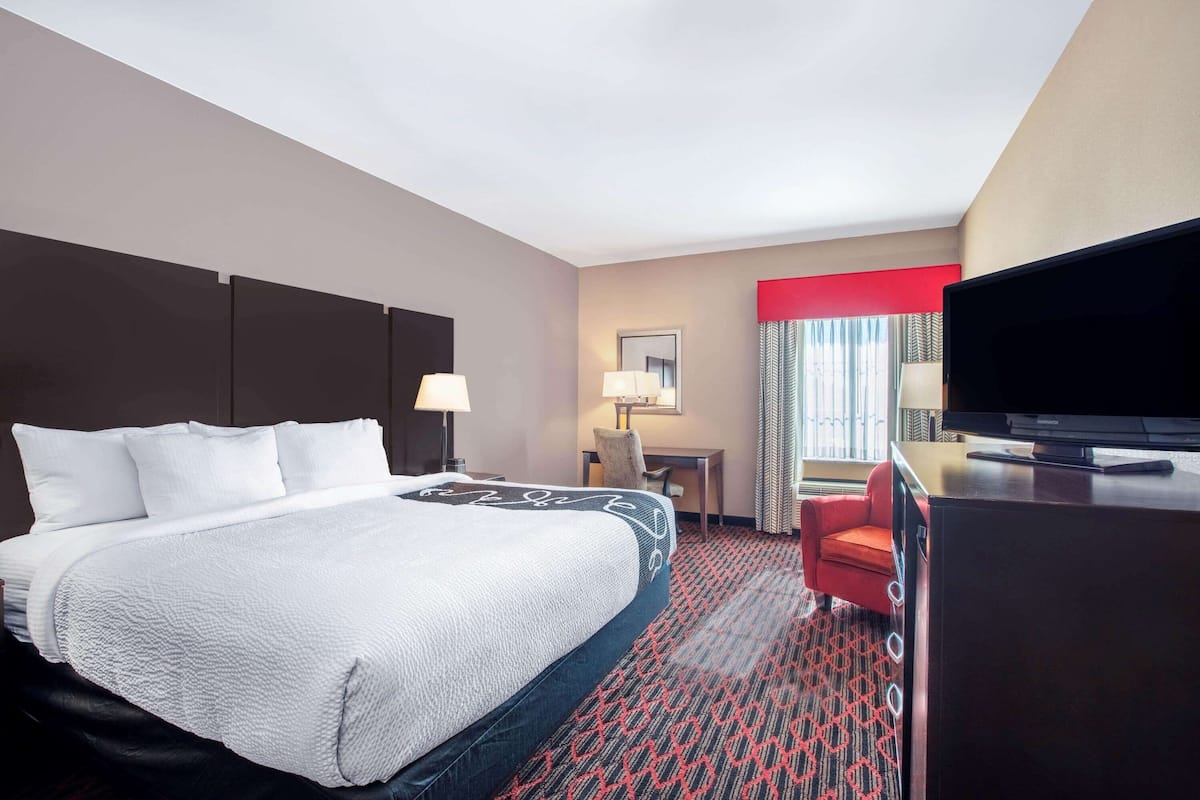 Una habitación de hotel con una cama grande, un escritorio, un televisor y una silla roja.
