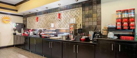 A hotel breakfast area with a counter, coffee machines, and food dispensers.