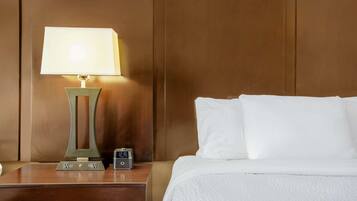 A neatly made bed with white linens, a bedside table with a lamp, and a digital clock.