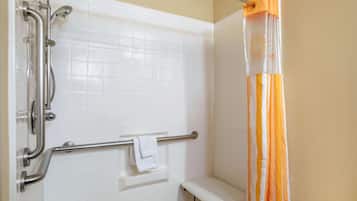 A bathroom with white tiled walls, a shower with a handheld showerhead, a grab bar, and a bench.