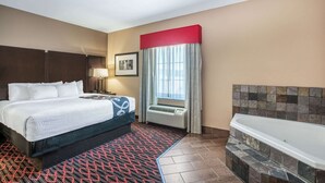 A hotel room with a large bed, a bathroom with a bathtub, a window with curtains, and a wall-mounted air conditioner. - La Quinta Inn & Suites by Wyndham Conway (Conway)