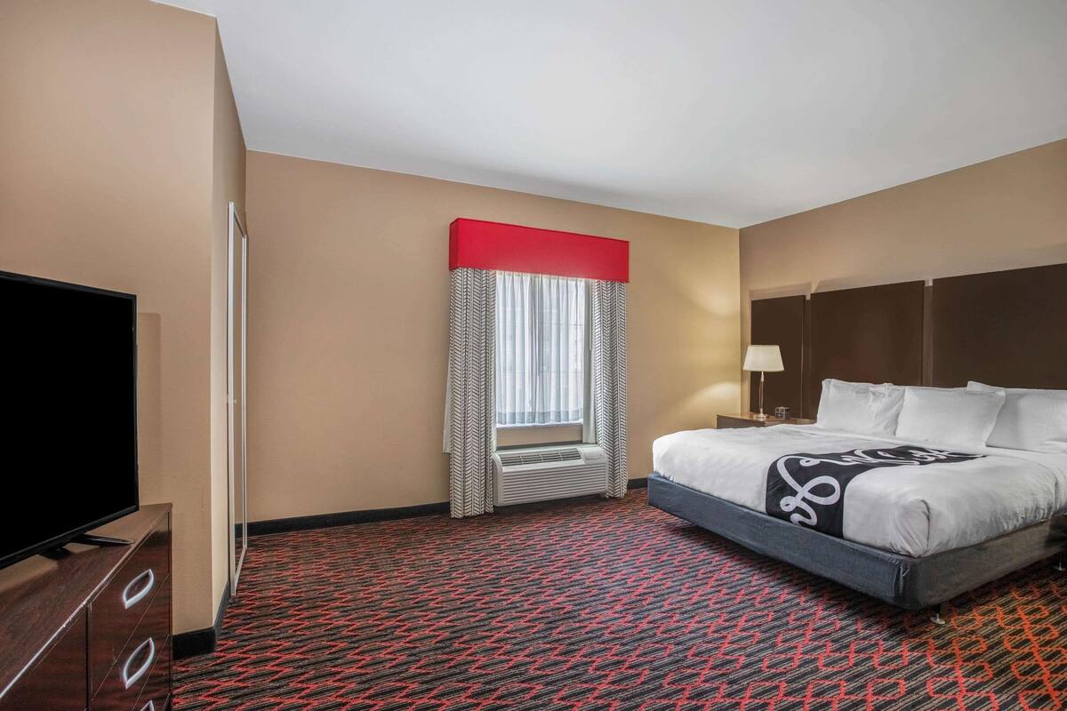 Una habitación de hotel con cama, televisor, calefacción y ventana con cortinas.
