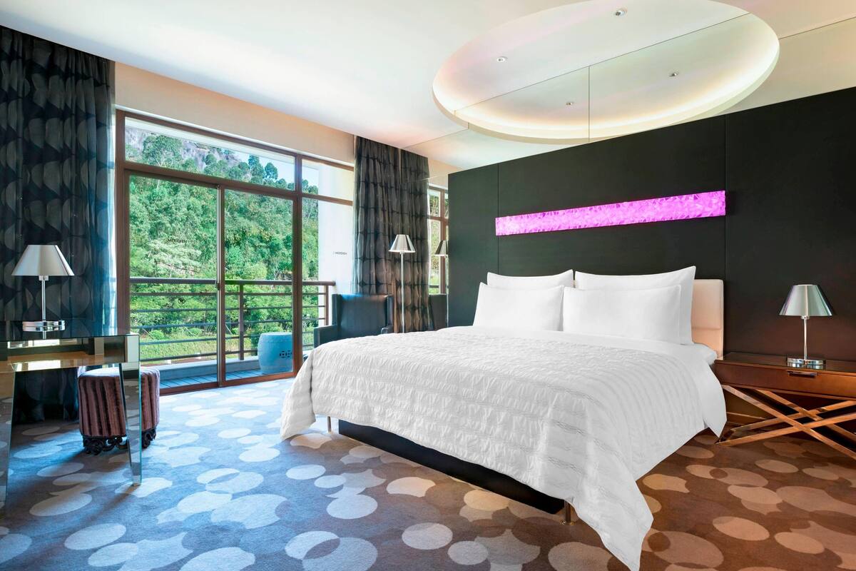 A modern hotel room with a large bed, a desk, and a view of the outdoors.