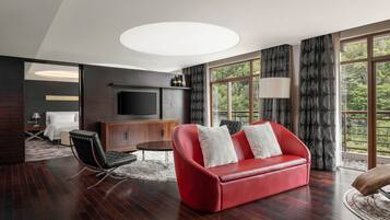 A modern living room with a red leather sofa, a flat-screen TV, and a large window with curtains.