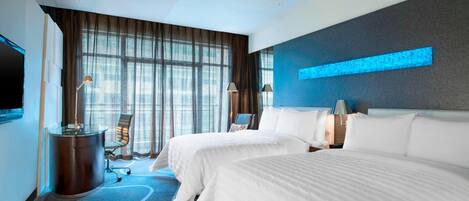 A hotel room with two beds, a desk, a chair, a TV, and large windows with curtains.