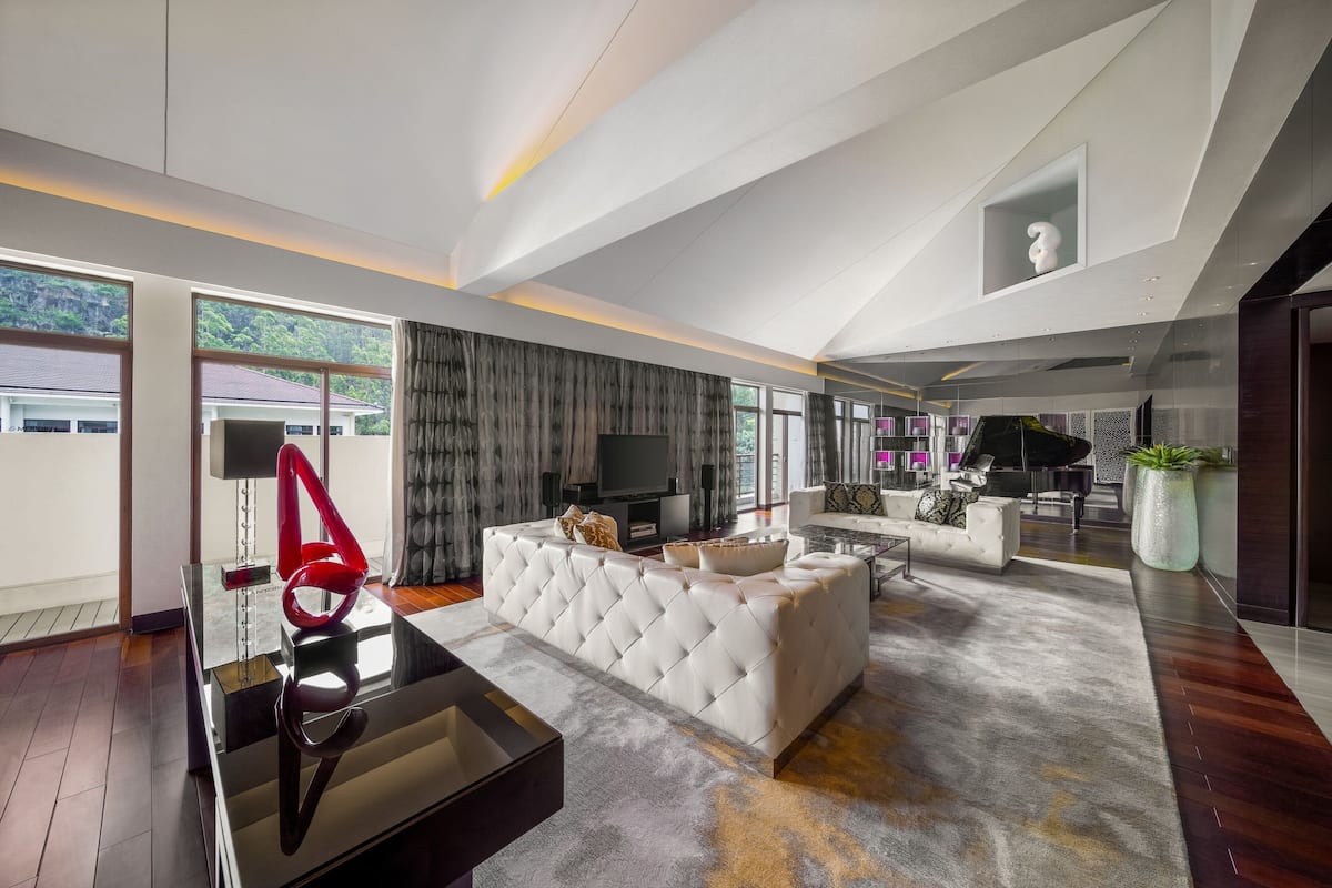A spacious living room with a large sectional sofa, a glass coffee table, and a piano.