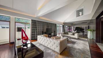 A spacious living room with a large sectional sofa, a glass coffee table, and a piano.