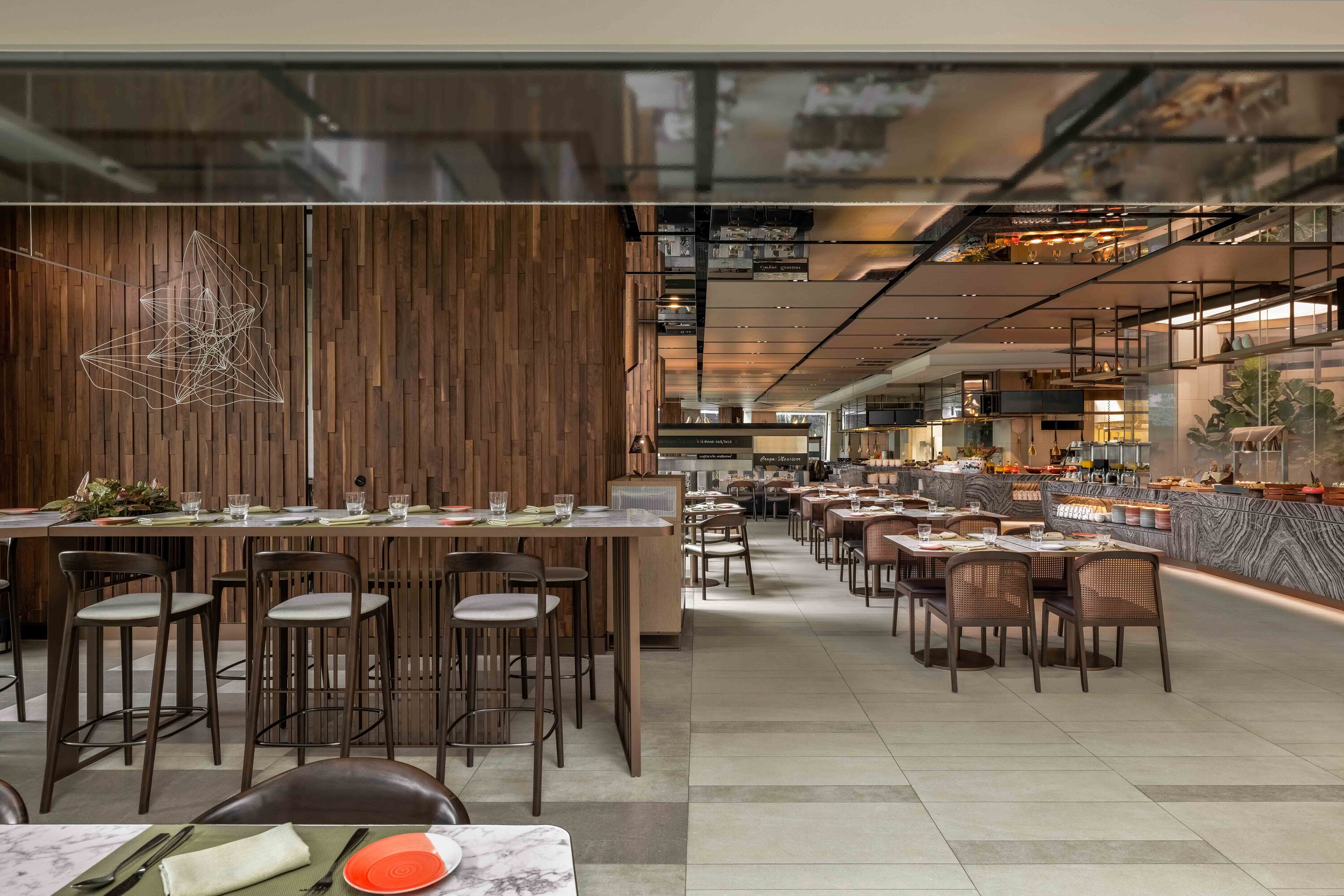 A modern restaurant with wooden panel walls, a central bar area, and multiple dining tables and chairs.