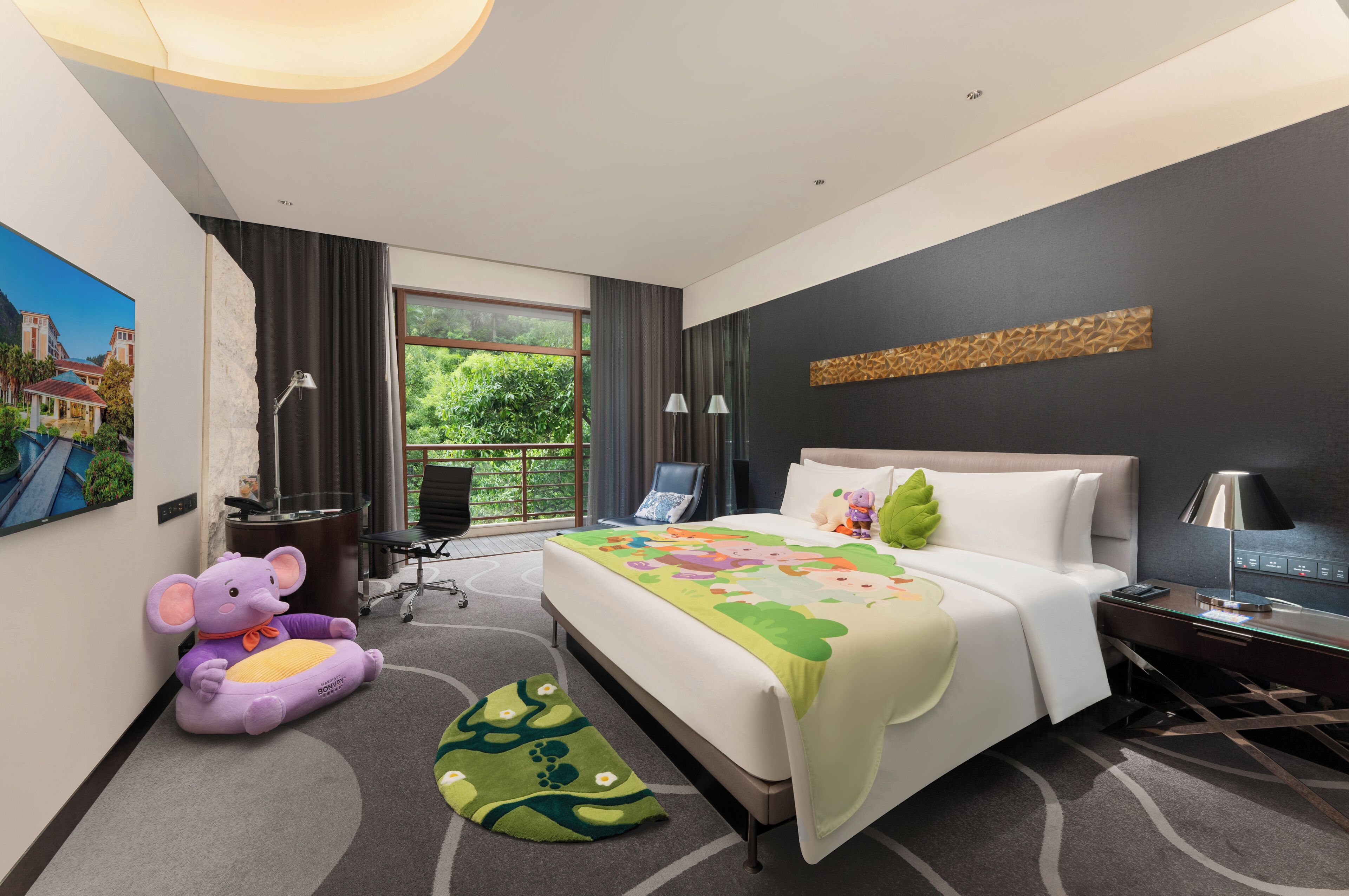 A hotel room with a bed, a desk, a chair, a large window, and a view of greenery.