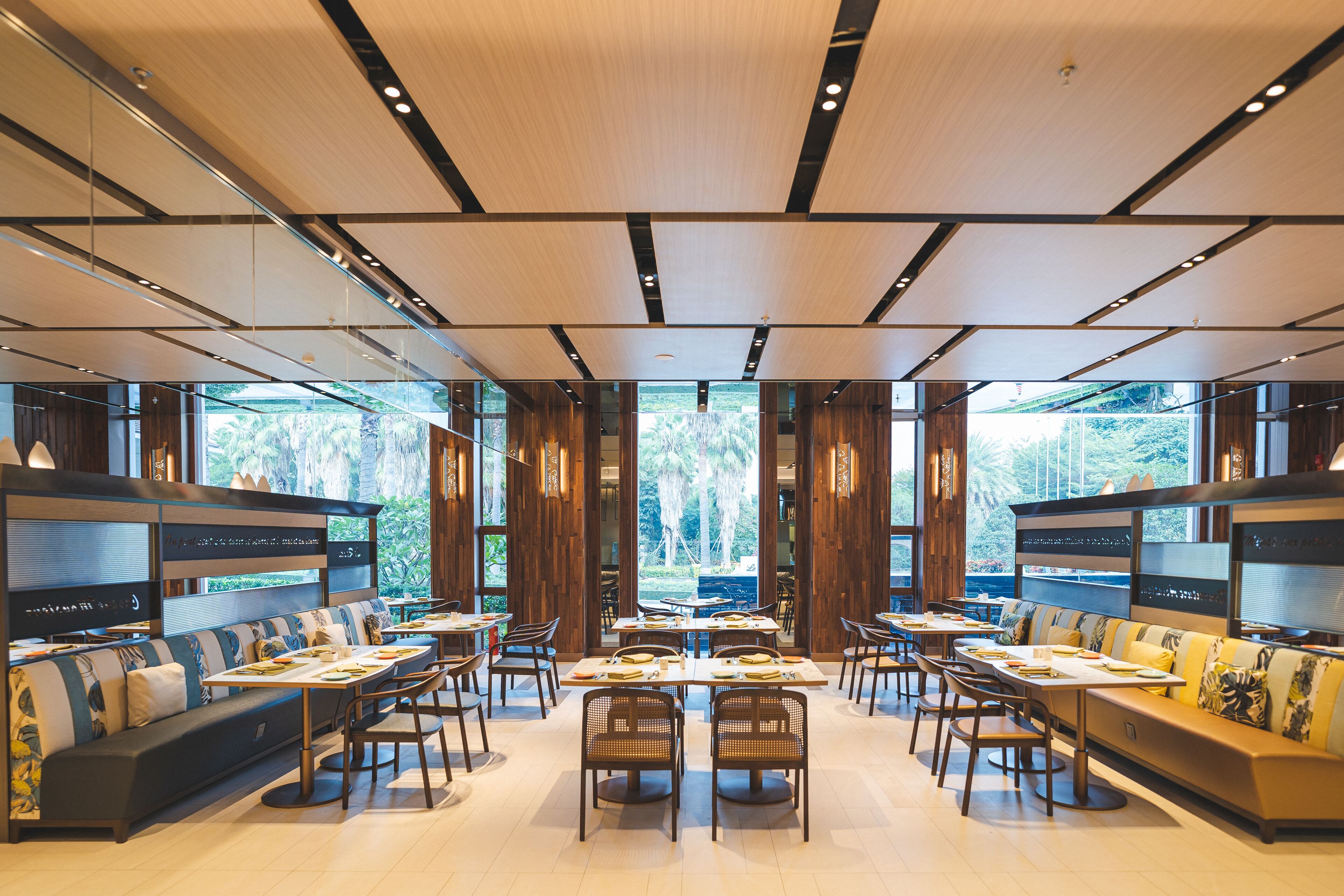 A modern restaurant with a central dining area, booths, and a view of the outdoors.