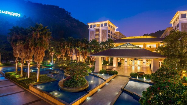 Un hotel con piscina, palmeras y montañas al fondo.