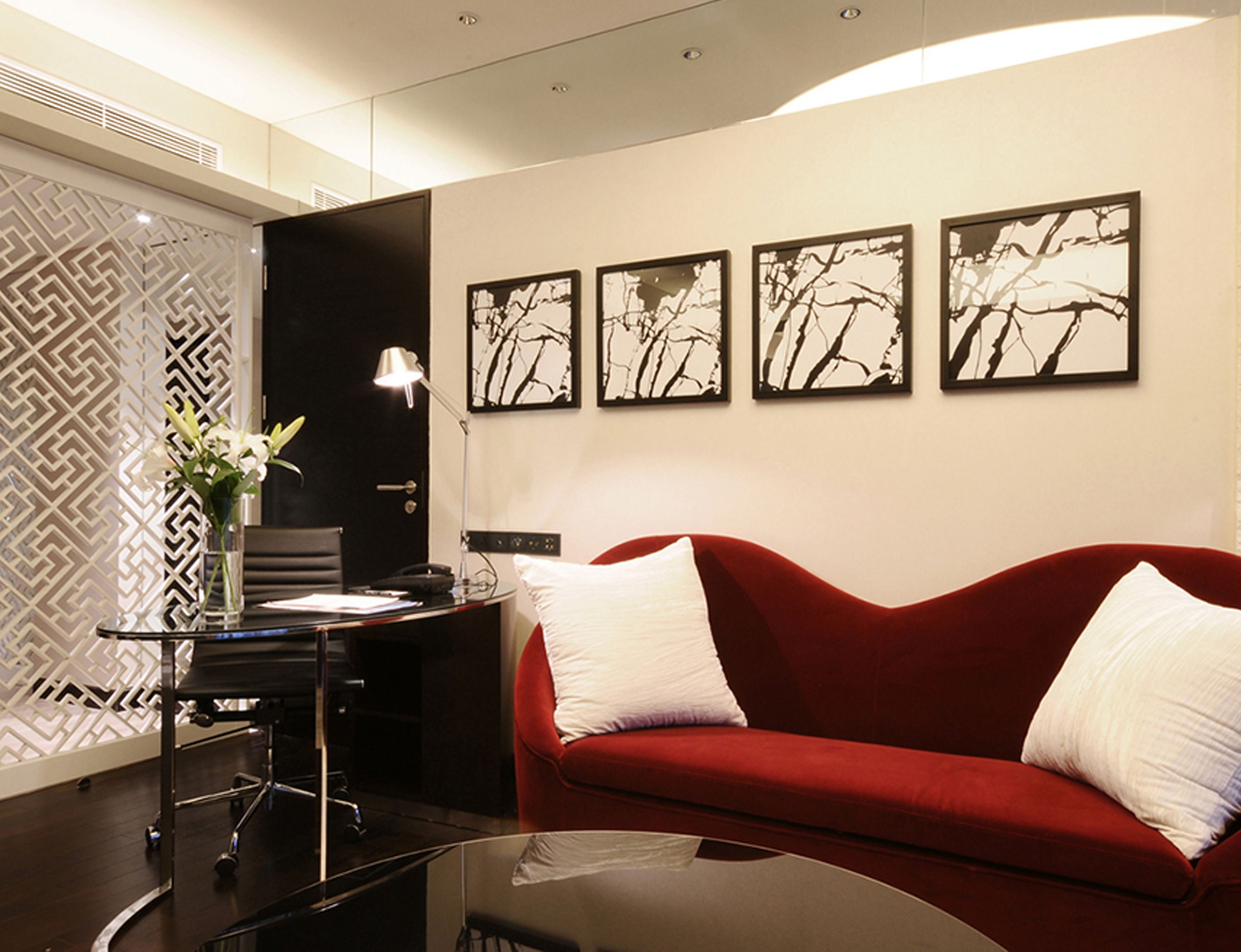 Een moderne kamer met een rode bank, een bureau met een lamp en vier ingelijste kunstwerken aan de muur.
