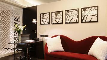 A modern room with a red sofa, a desk with a lamp, and four framed artworks on the wall.