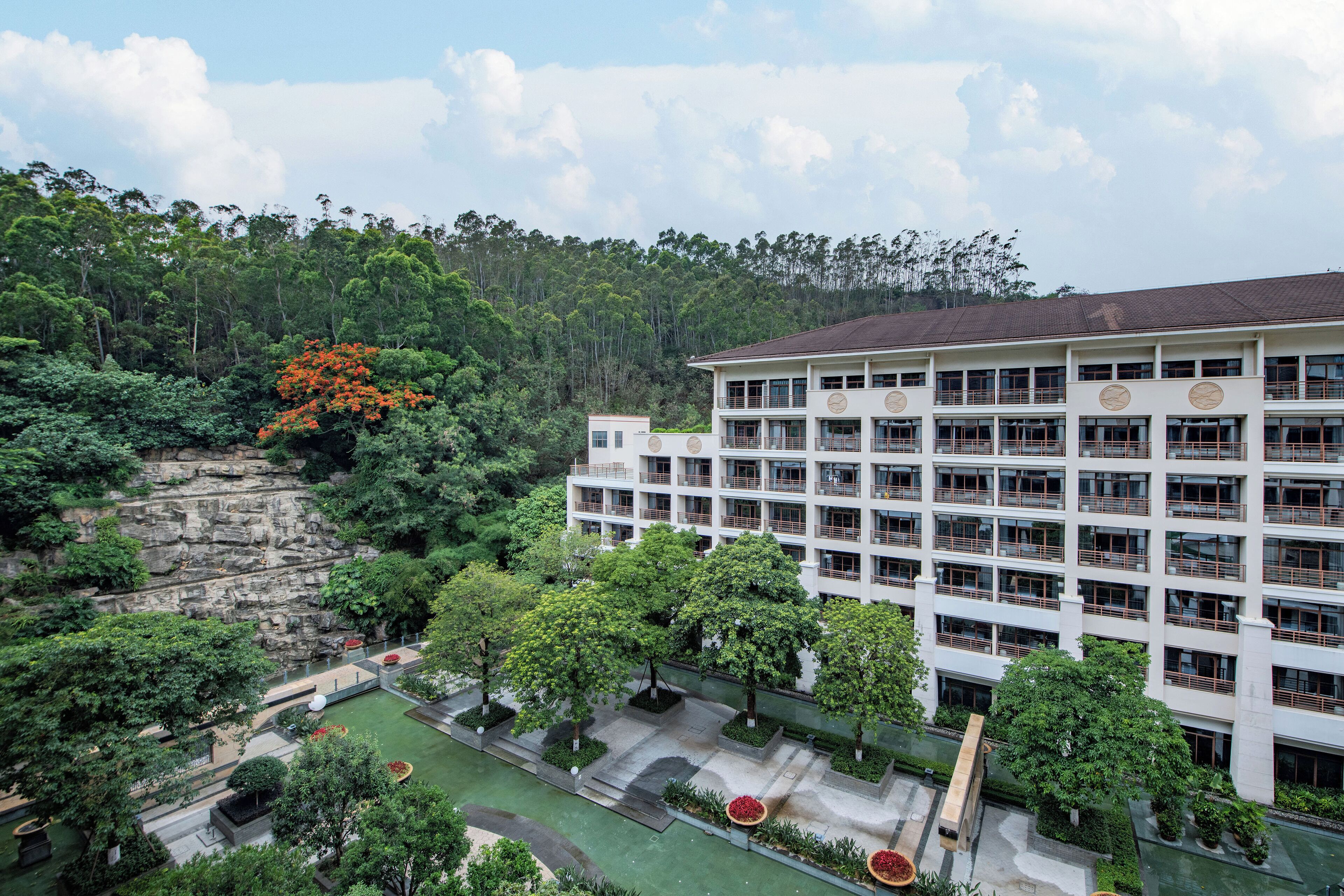A multi-story building with a modern architectural design, surrounded by lush greenery and a rocky cliff.