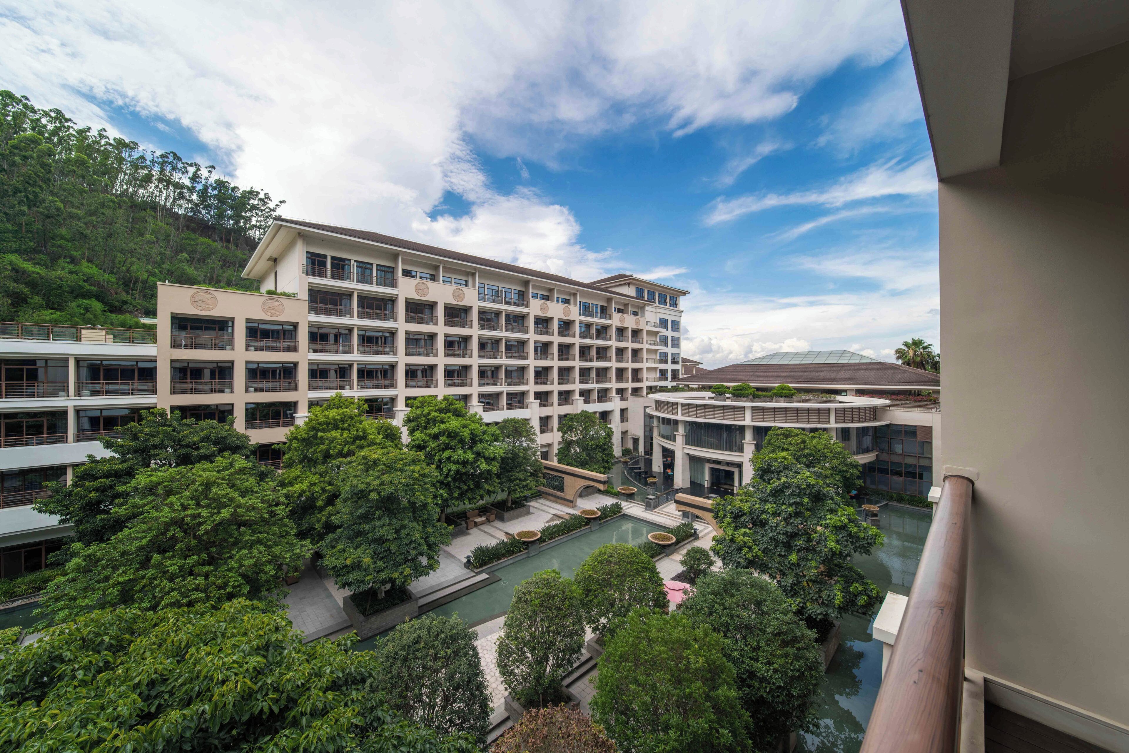 A multi-story hotel with a central courtyard, a swimming pool, and lush greenery.
